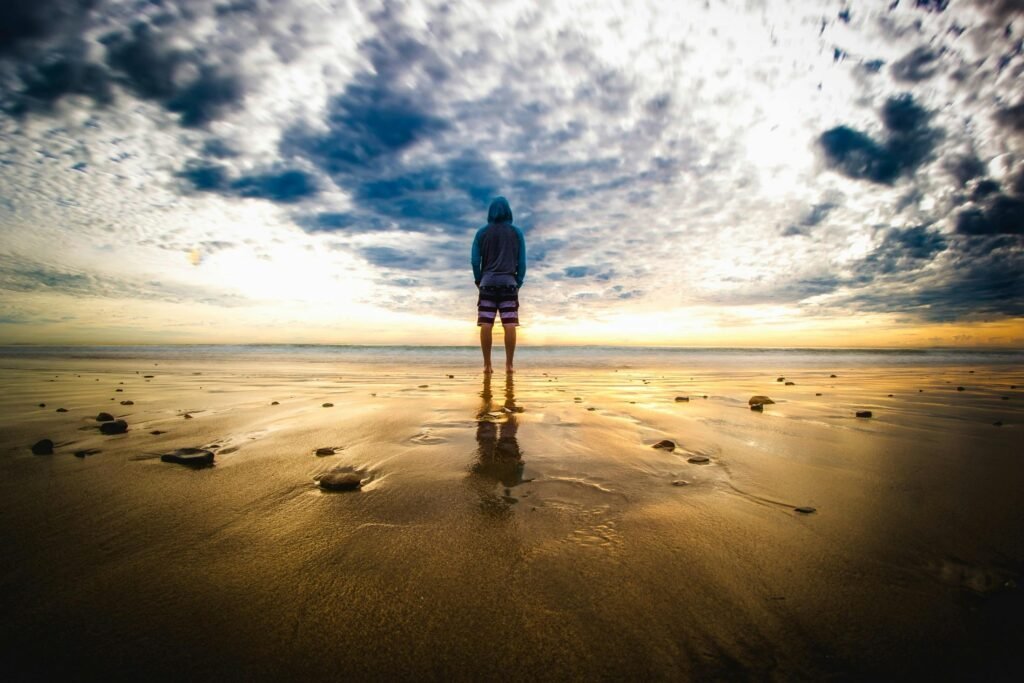About Tennis Unlocked A lone figure stands on a tranquil beach during a vivid sunset, reflecting on the wet sand.